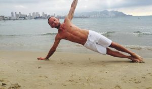 Side plank balance exercise on beach with urban coastal backdrop